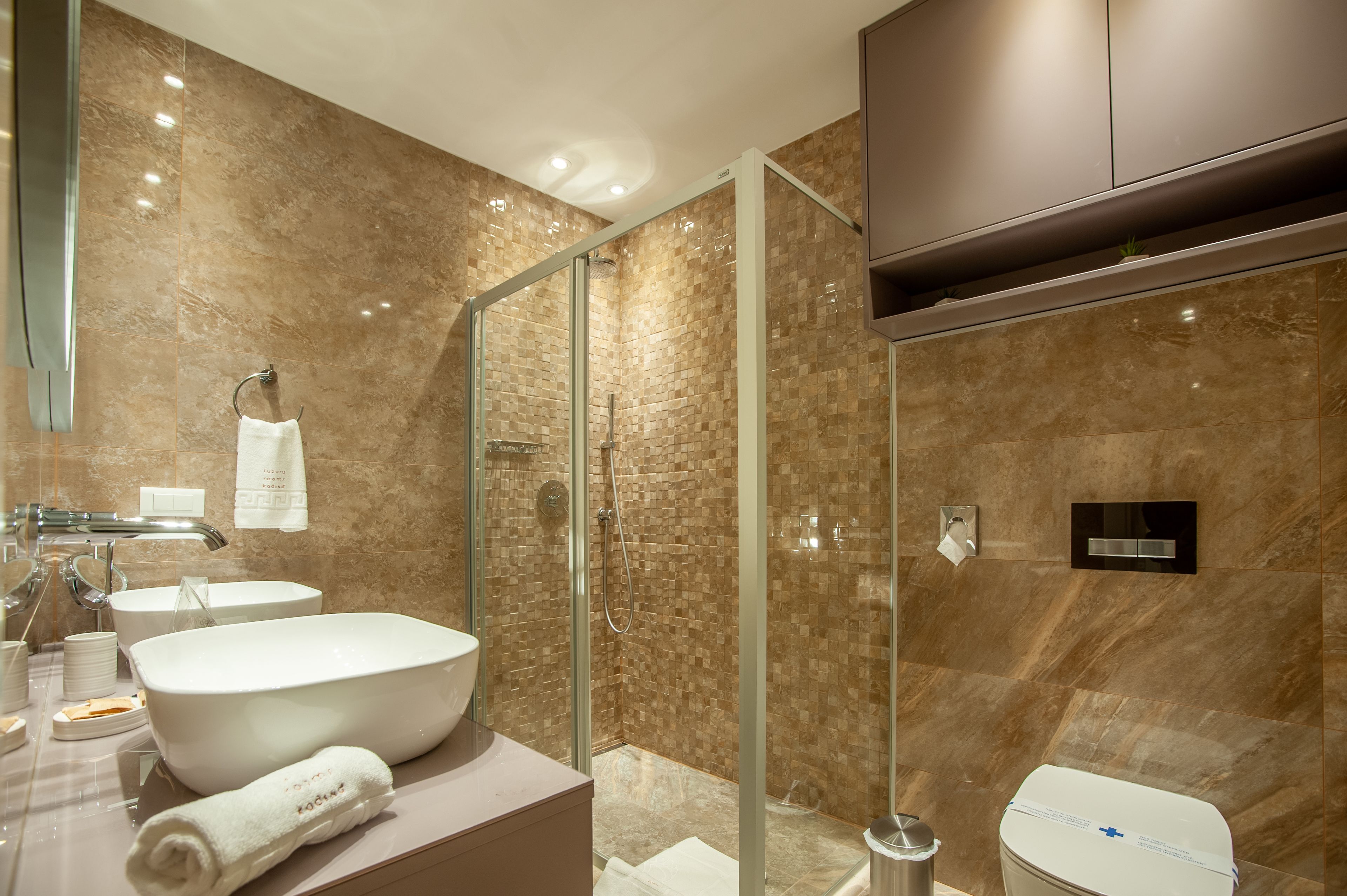 Un baño moderno con ducha de vidrio, un lavamanos grande de color blanco y un inodoro.