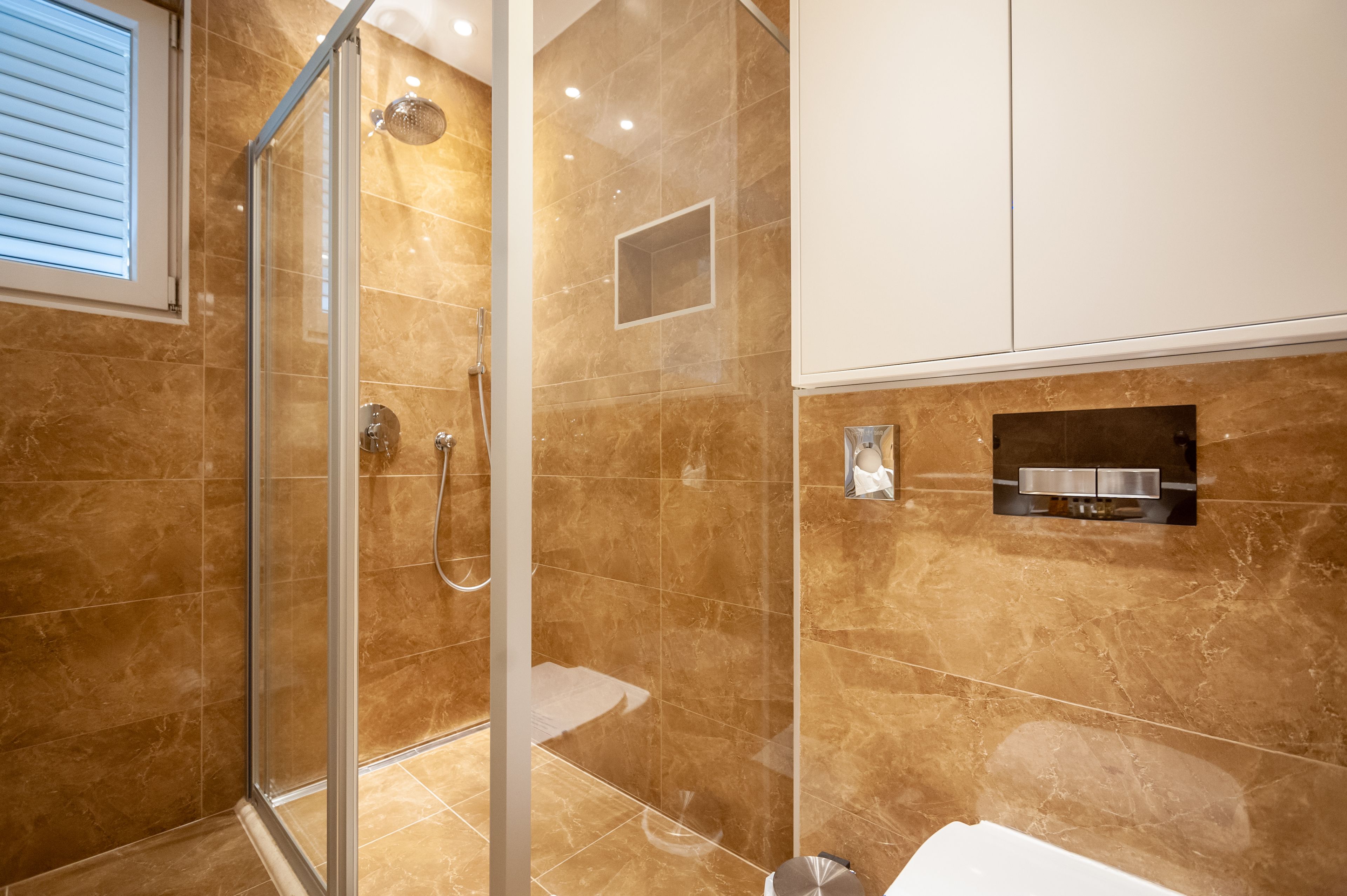 A modern bathroom with a glass-enclosed shower, marble walls, and a built-in sink.