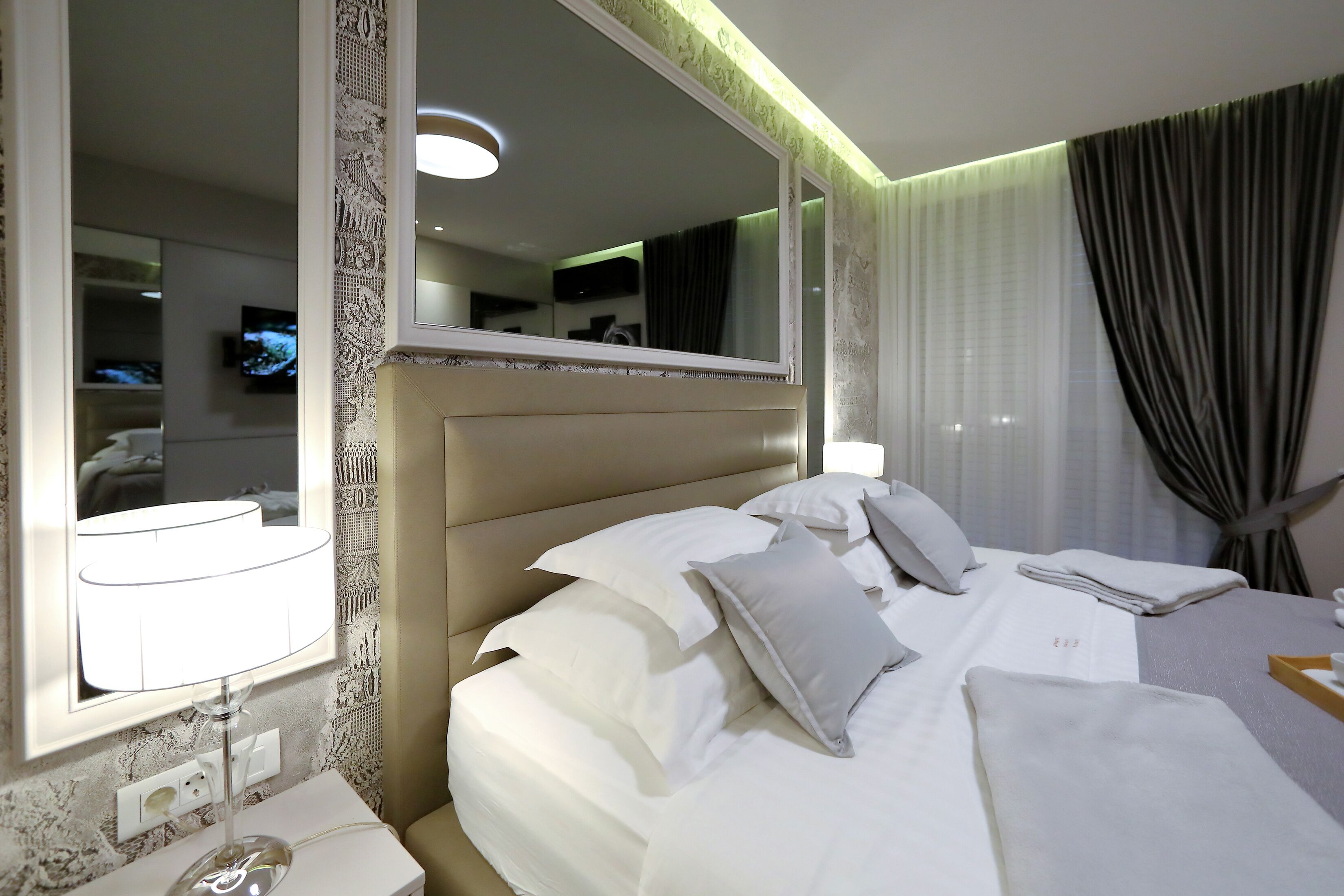 A hotel room with a large bed, a bedside table, a mirror, and a television in the background.