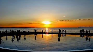Een zonsondergang boven een wateroppervlak, met mensen op een betegeld voetpad.