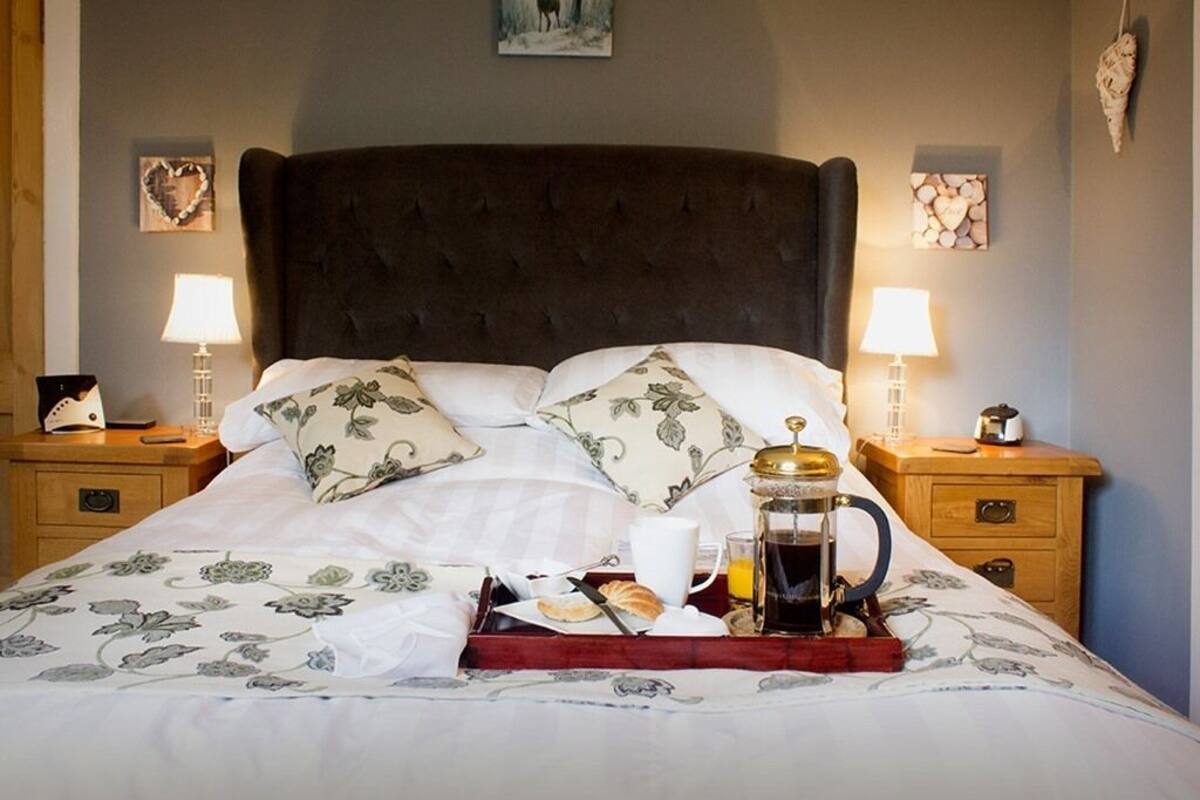 A neatly made bed with a tray of breakfast items, including a coffee pot, croissant, and orange juice.