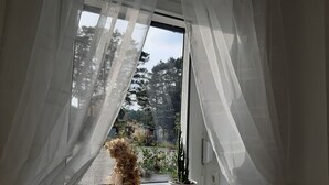 A room with a window covered by sheer curtains, a potted plant, and a vase with flowers on the windowsill. - Pension Mark (Hoyerswerda)
