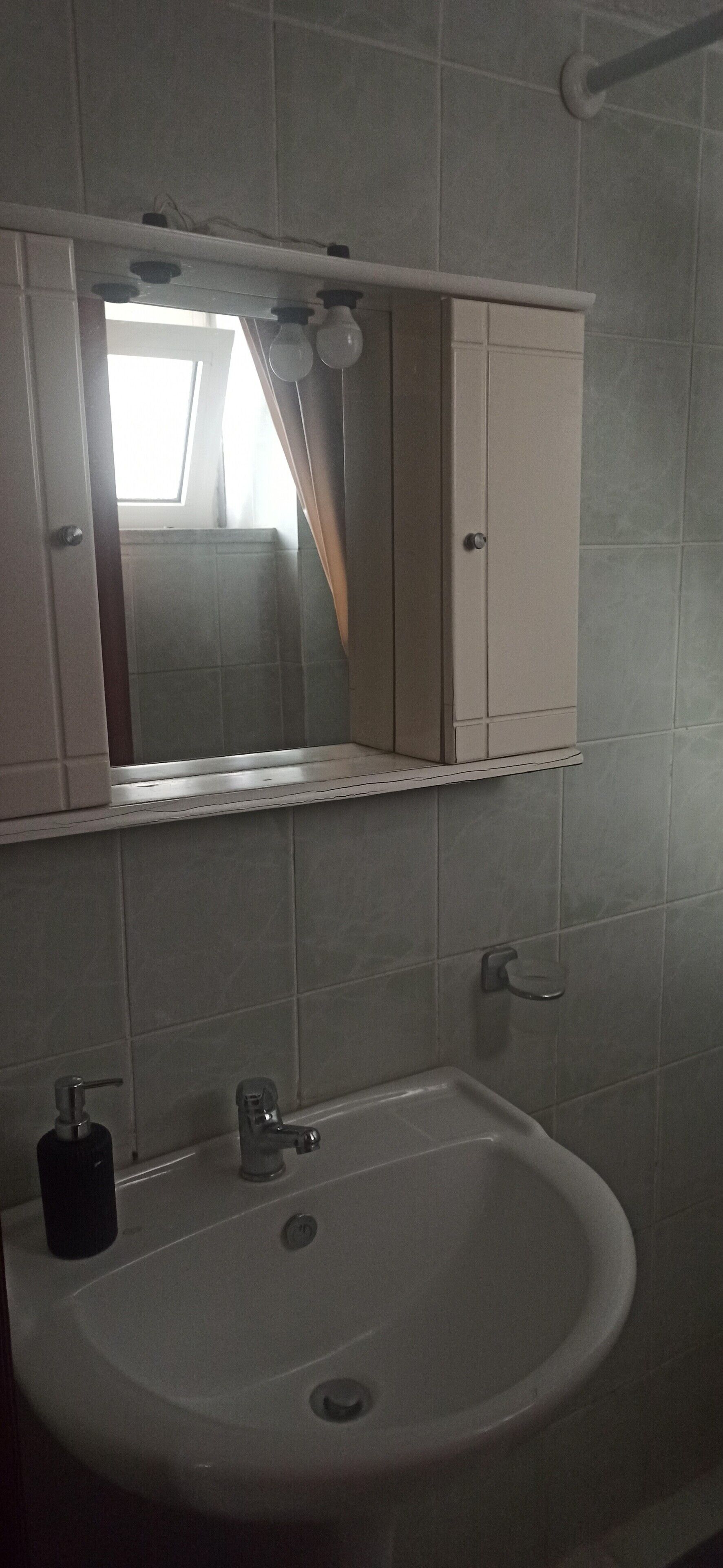 Et badeværelse med en hvid vask, et spejl og et skab over vasken.