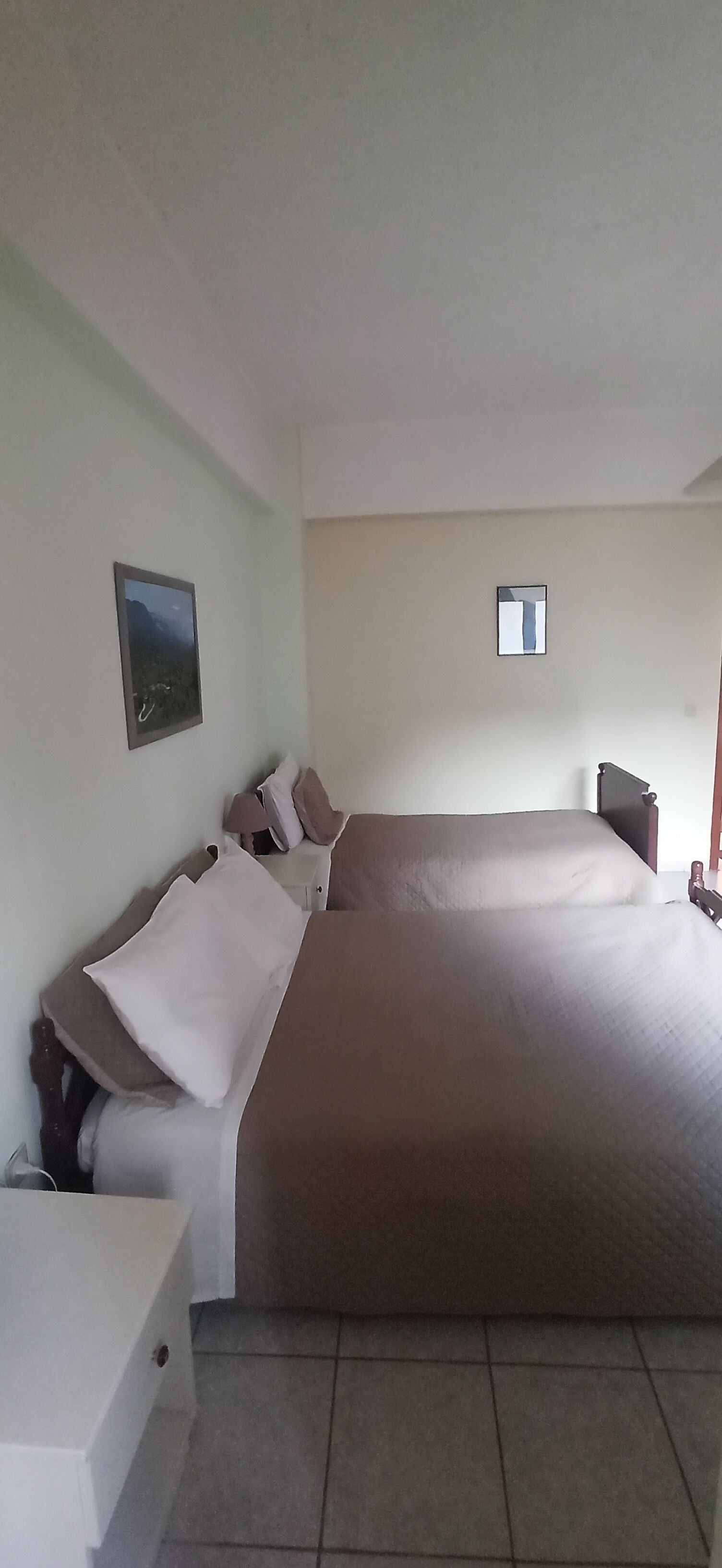 Une chambre avec un grand lit, une table de chevet, une chaise et une petite fenêtre.