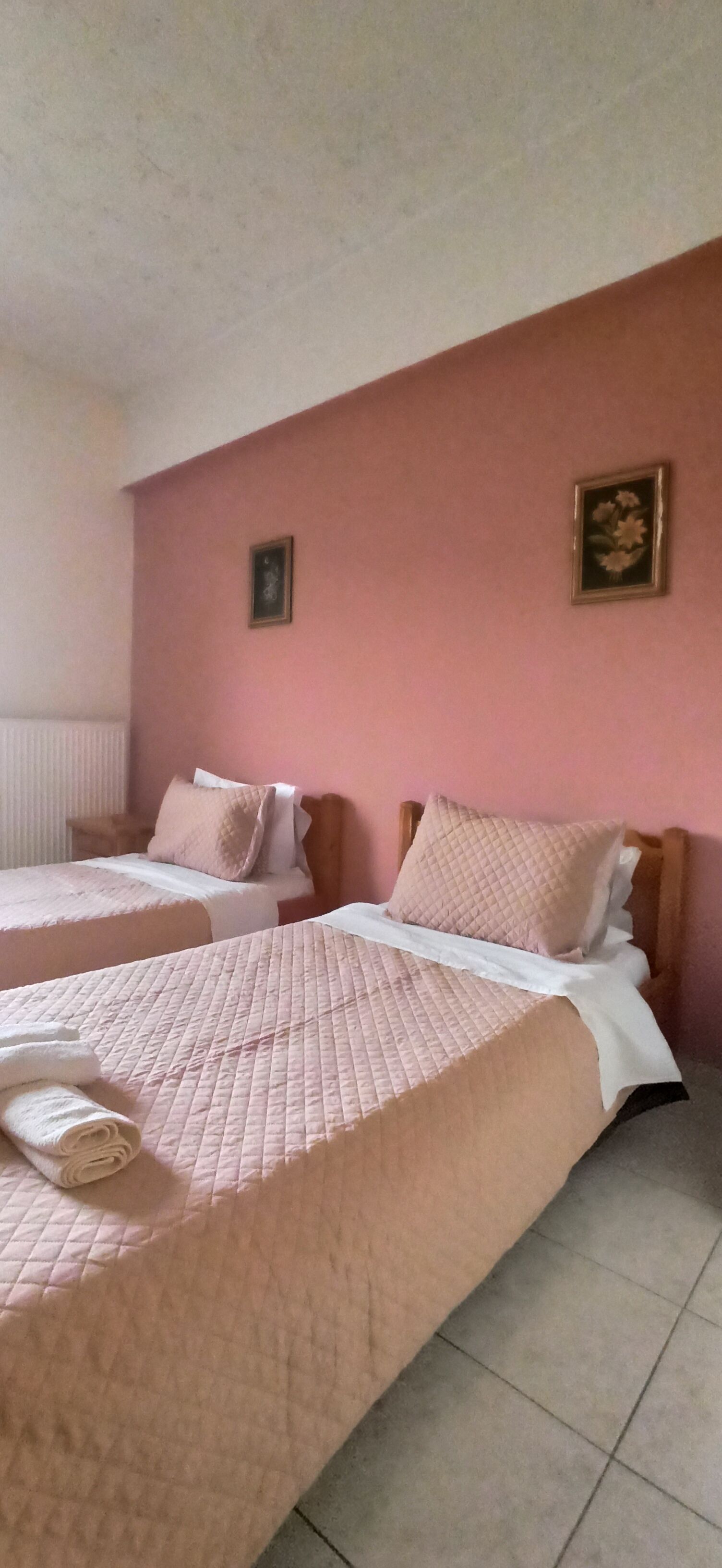 Habitación de hotel con dos camas, cada una con una colcha acolchada rosa y ropa de cama blanca.