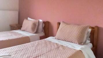 Habitación de hotel con dos camas, cada una con una colcha acolchada rosa y ropa de cama blanca.