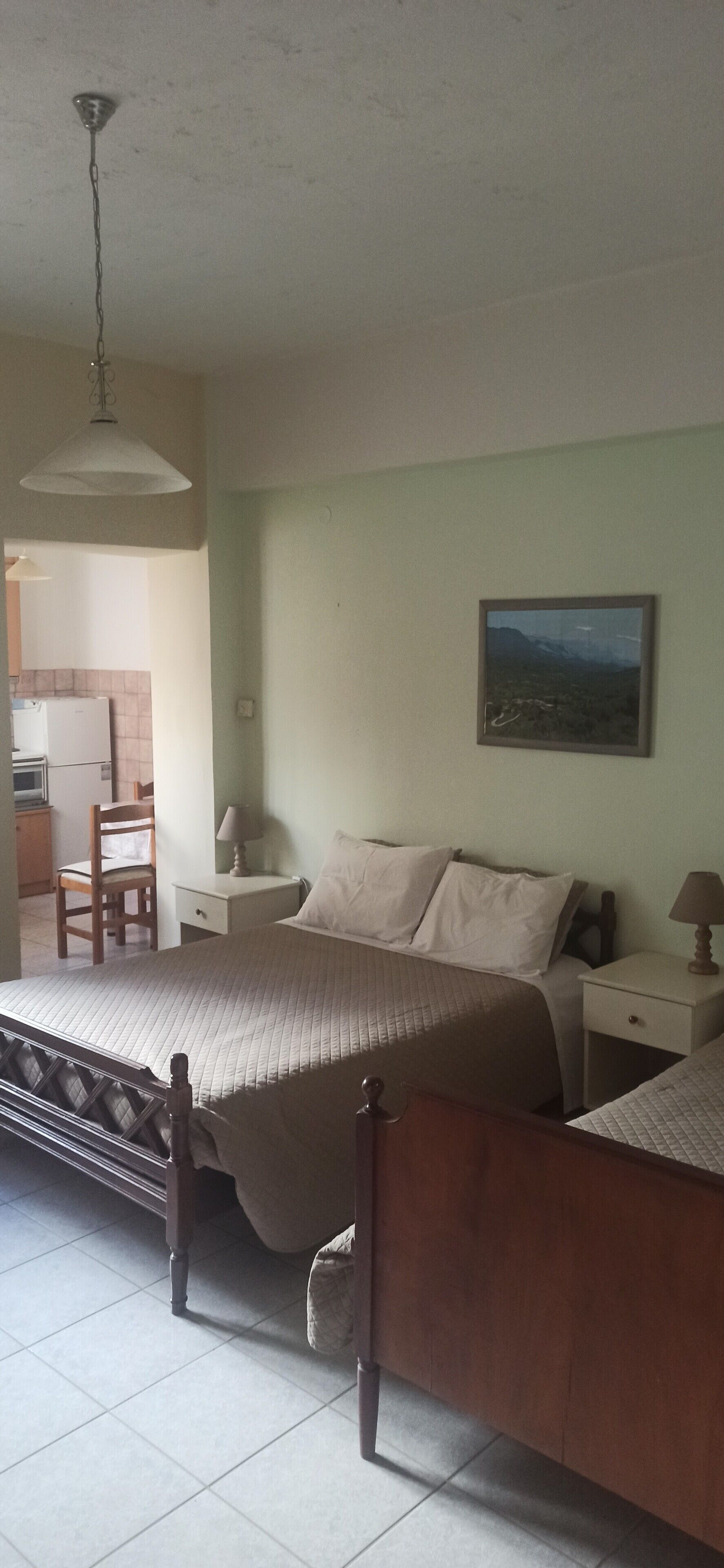 Un dormitorio con cama, mesitas de noche, una silla, una lámpara colgante y un cuadro en la pared.