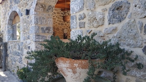 A stone building with arched doorways and a large potted plant in the foreground. - Windy Place (Amari)