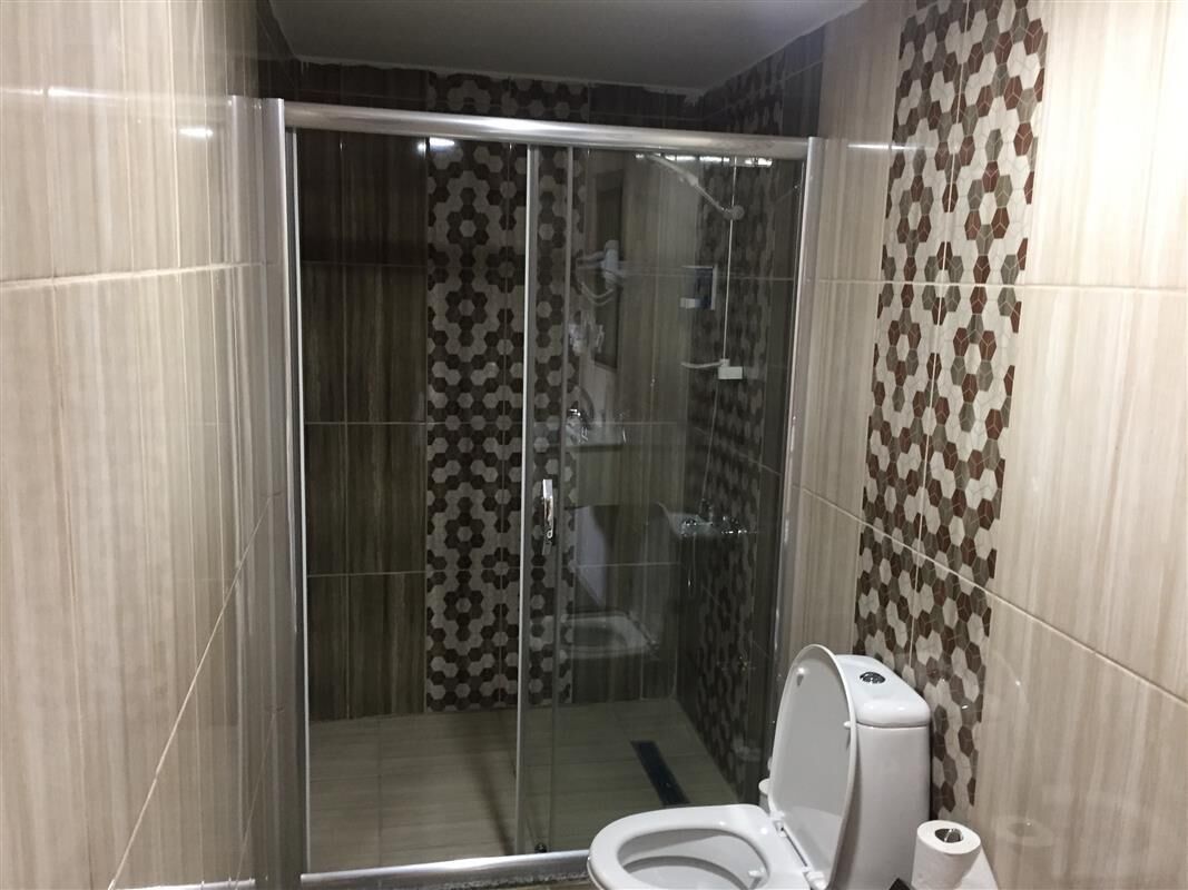 A bathroom with a glass-enclosed shower, a toilet, and patterned tiles.