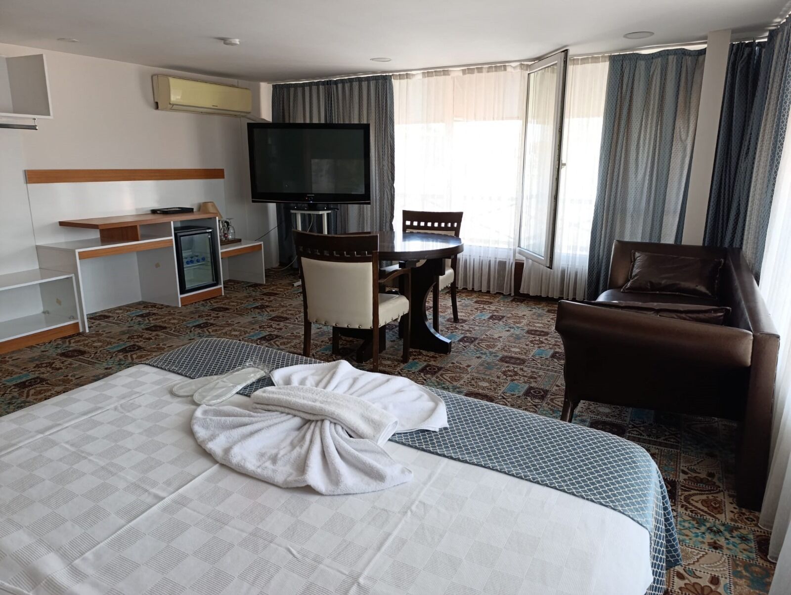 A hotel room with a bed, a desk, a chair, a TV, and a window with curtains.