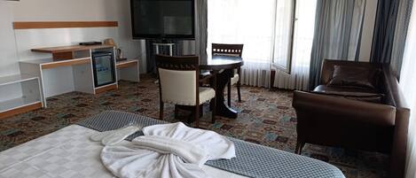 A hotel room with a bed, a desk, a chair, a TV, and a window with curtains.