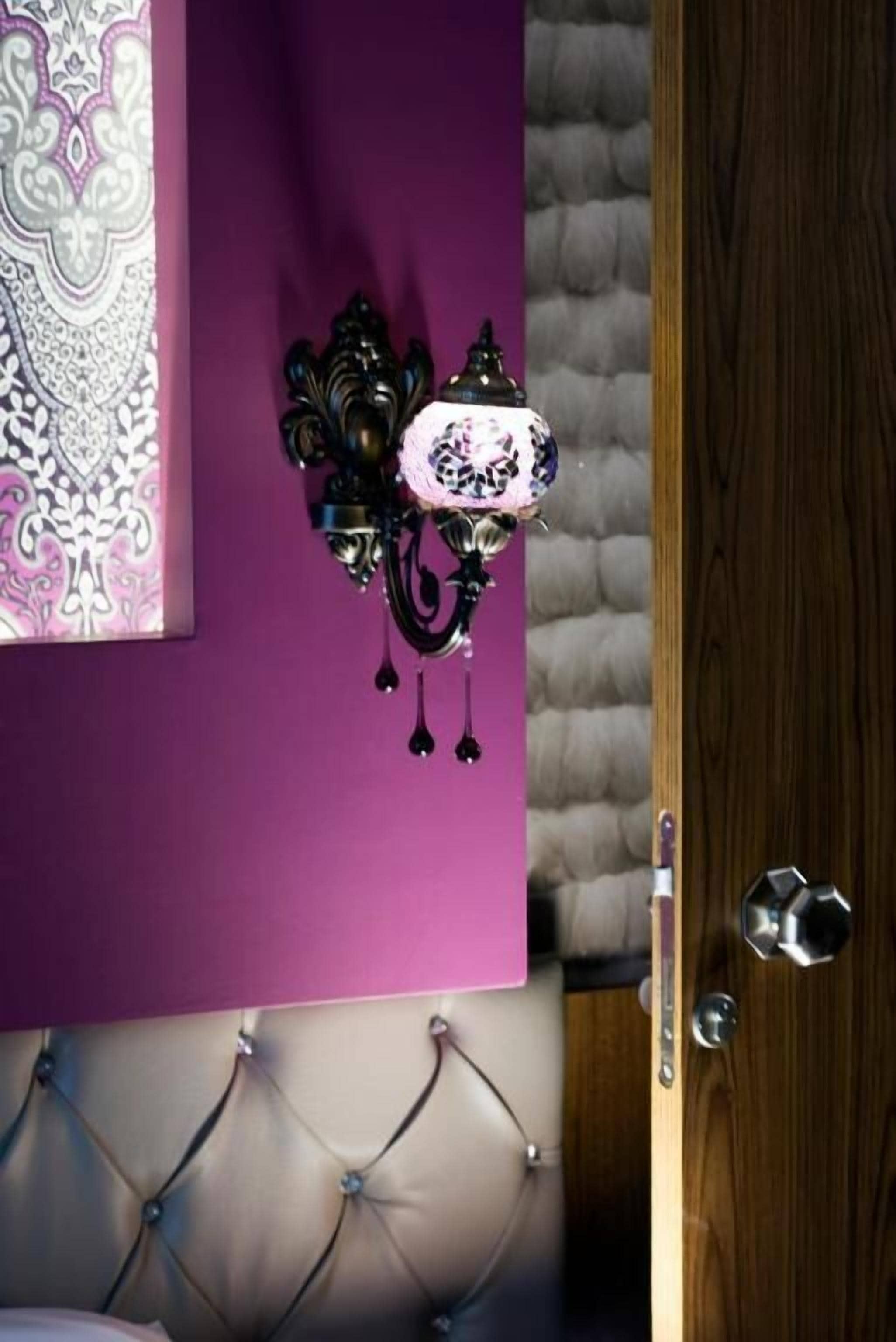A room with a purple wall, a decorative wall hanging, a tufted headboard, and a wooden door.