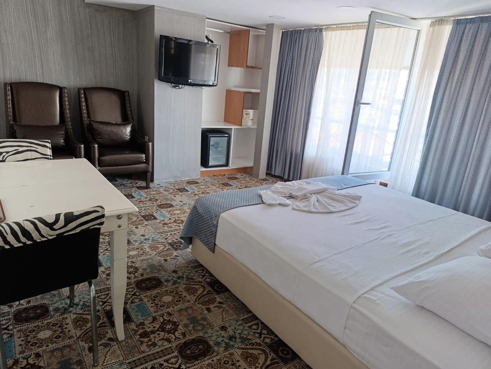 Een hotelkamer met een bed, een bureau, twee stoelen, een televisie en een kleine koelkast.