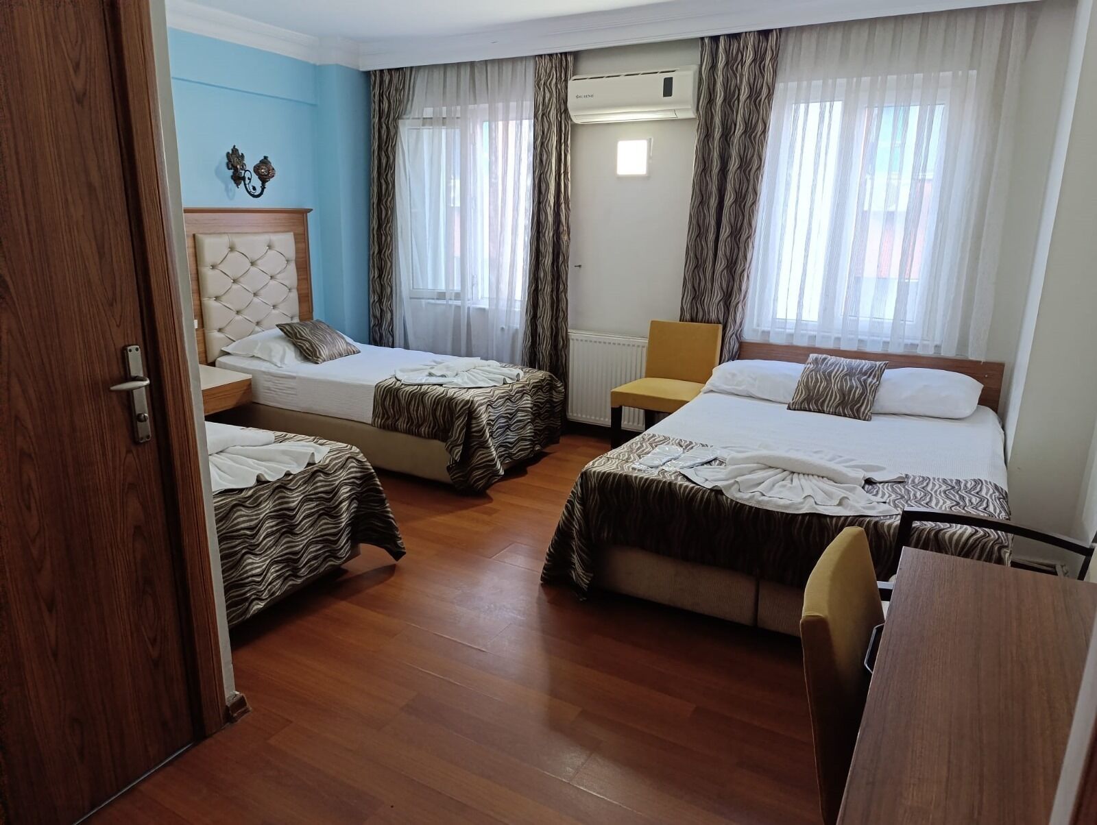 A hotel room with three beds, a wooden floor, a chair, and an air conditioning unit.