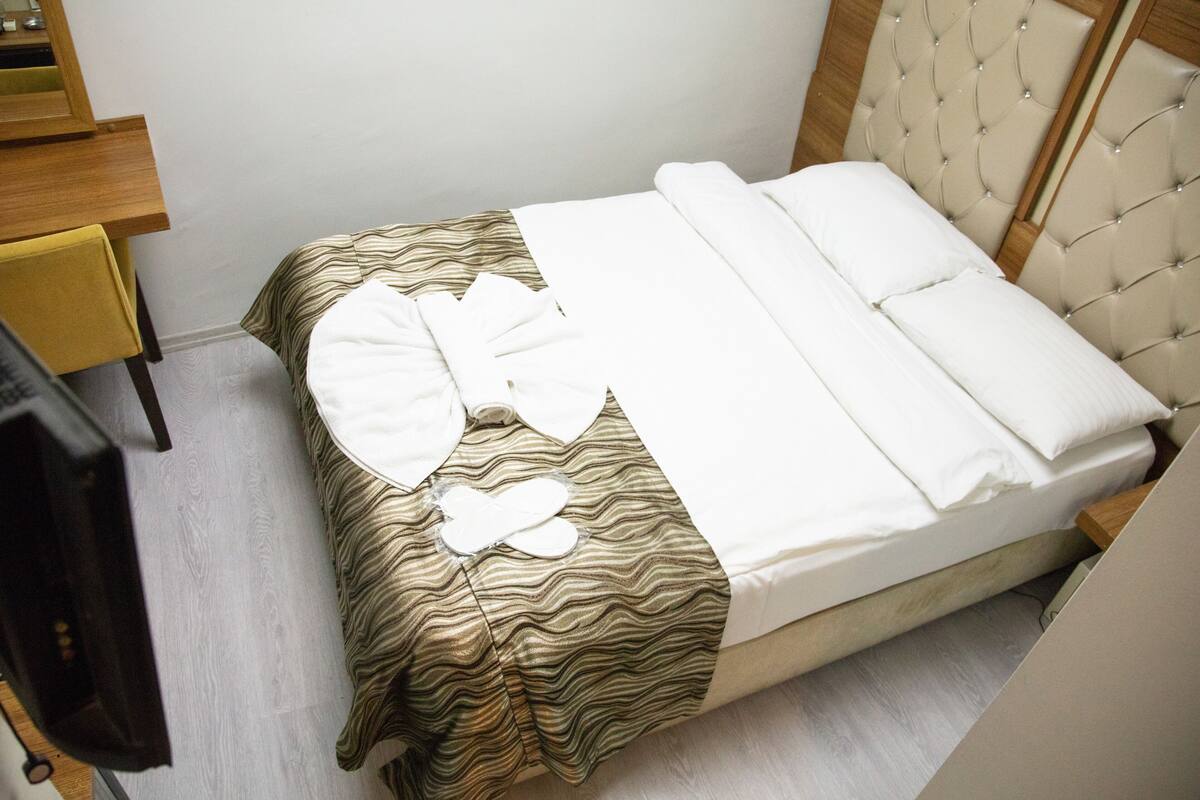 A neatly made bed with a striped bedspread and white pillows, a wooden nightstand with a lamp, and a wooden headboard.