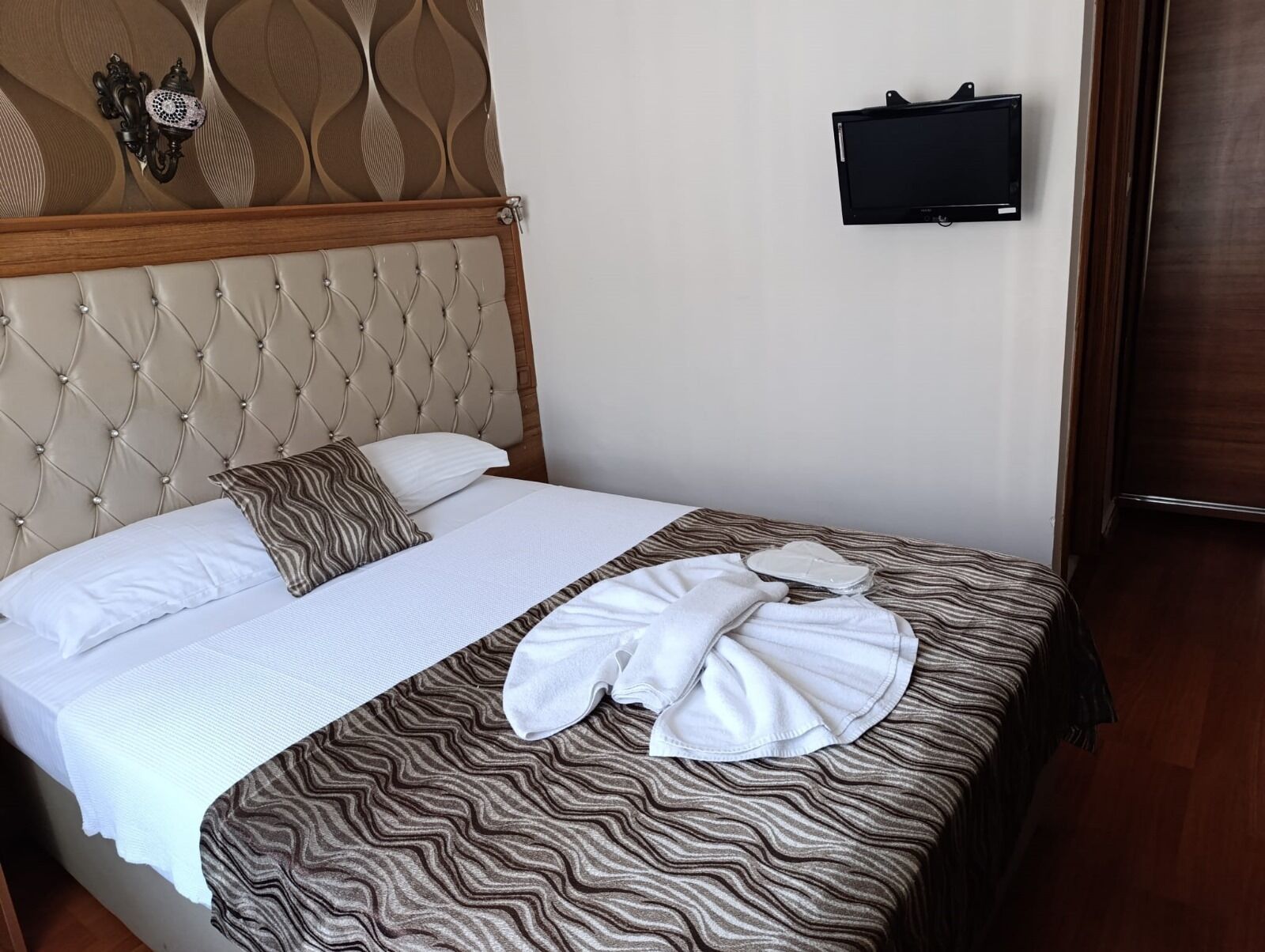 A neatly made bed with a striped bedspread, a white pillow, and a brown throw pillow. A flat-screen TV is mounted on the wall above the bed.