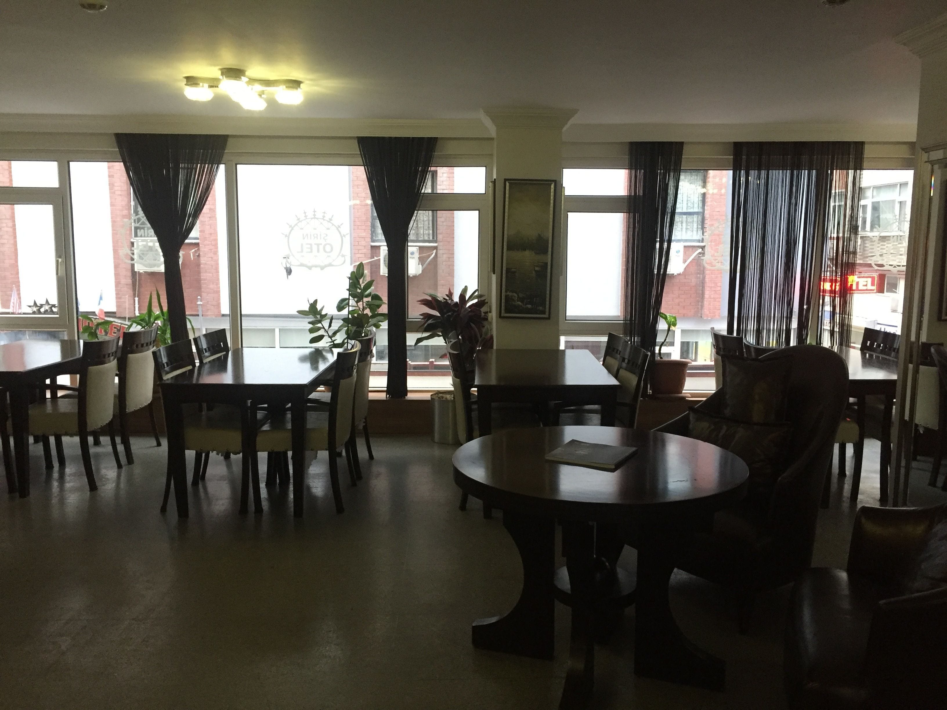 Un vaste espace dédié à la salle à manger, avec une grande table ronde et plusieurs chaises, de grandes fenêtres avec des rideaux et des plantes en pot.