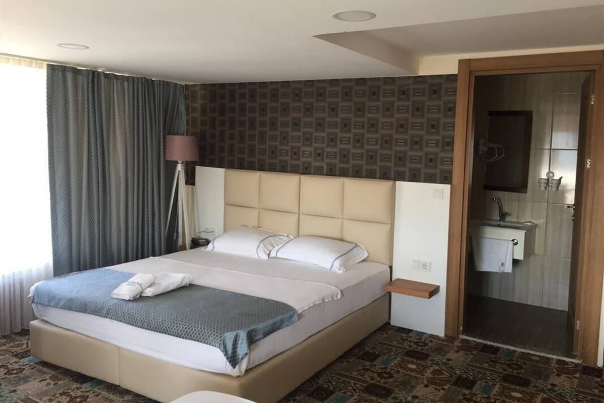 A hotel room with a large bed, a bedside table, a lamp, a bathroom with a sink and mirror, and patterned wallpaper.