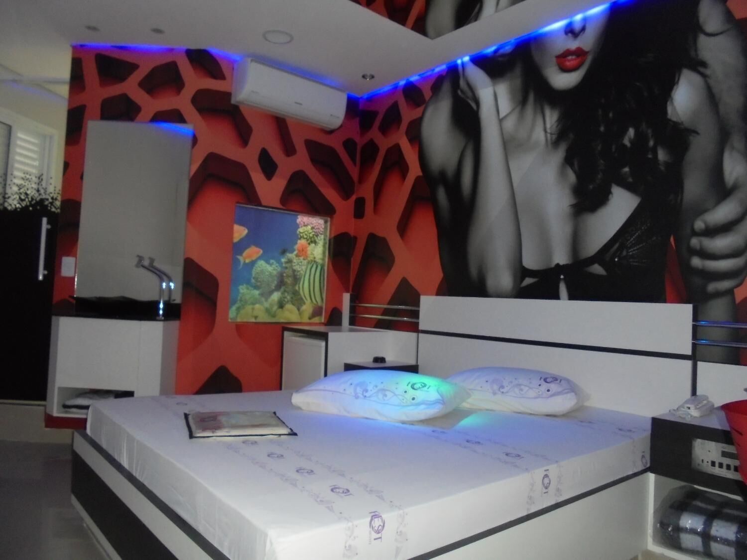 Quarto moderno com uma cama, mesa de cabeceira, prateleira na parede e um pôster grande.