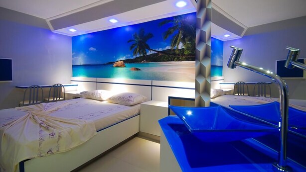 Un dormitorio con cama, mesita de noche, lavamanos y un mural de playa en la pared.