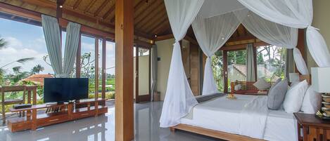 Quarto espaçoso com uma cama grande, televisão e varanda com vista para palmeiras.