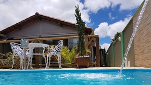 Una piscina con mesa y sillas, una planta en maceta y un edificio al fondo.