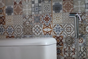 A bathroom with a white toilet and a shower with a chrome faucet. The walls are tiled with various geometric and floral patterns. - Pousada Makutta (Ouro Preto)