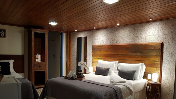 Un dormitorio con cabecera de madera, cama con ropa de cama blanca y gris, mesita de noche con lámpara y baldosas de suelo estampadas.