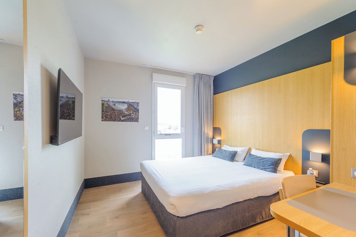 Ein Hotelzimmer mit Bett, Nachttisch, Lampe und einem Fenster mit Vorhängen.