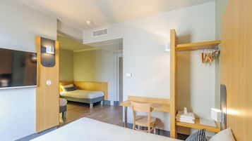 A modern hotel room with a bed, a desk, a chair, a TV, a coat rack, and a bathroom door.