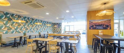 A modern restaurant interior with patterned walls, multiple dining tables and chairs, and a large poster on the wall.