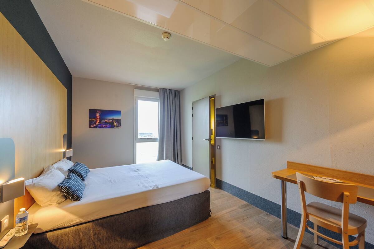 Ein Hotelzimmer mit einem Bett, einem Schreibtisch, einem Stuhl, einem Fernseher und einem Fenster.