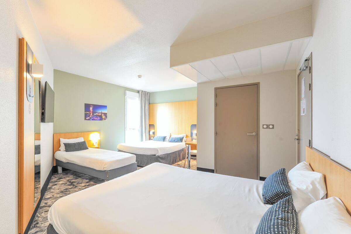 Ein Hotelzimmer mit zwei Betten, einem Schreibtisch, einem Stuhl, einer Tür und einem an der Wand befestigten Fernseher.