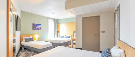 A hotel room with two beds, a desk, a chair, a door, and a wall-mounted TV.