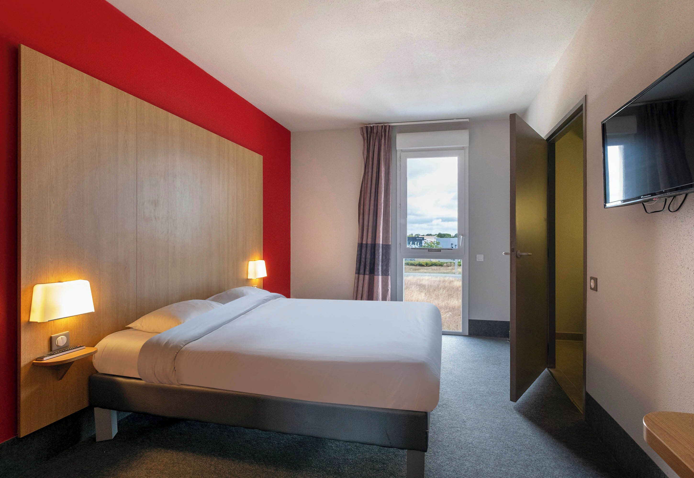 A hotel room with a bed, bedside lamps, a TV, and a door leading to a balcony.