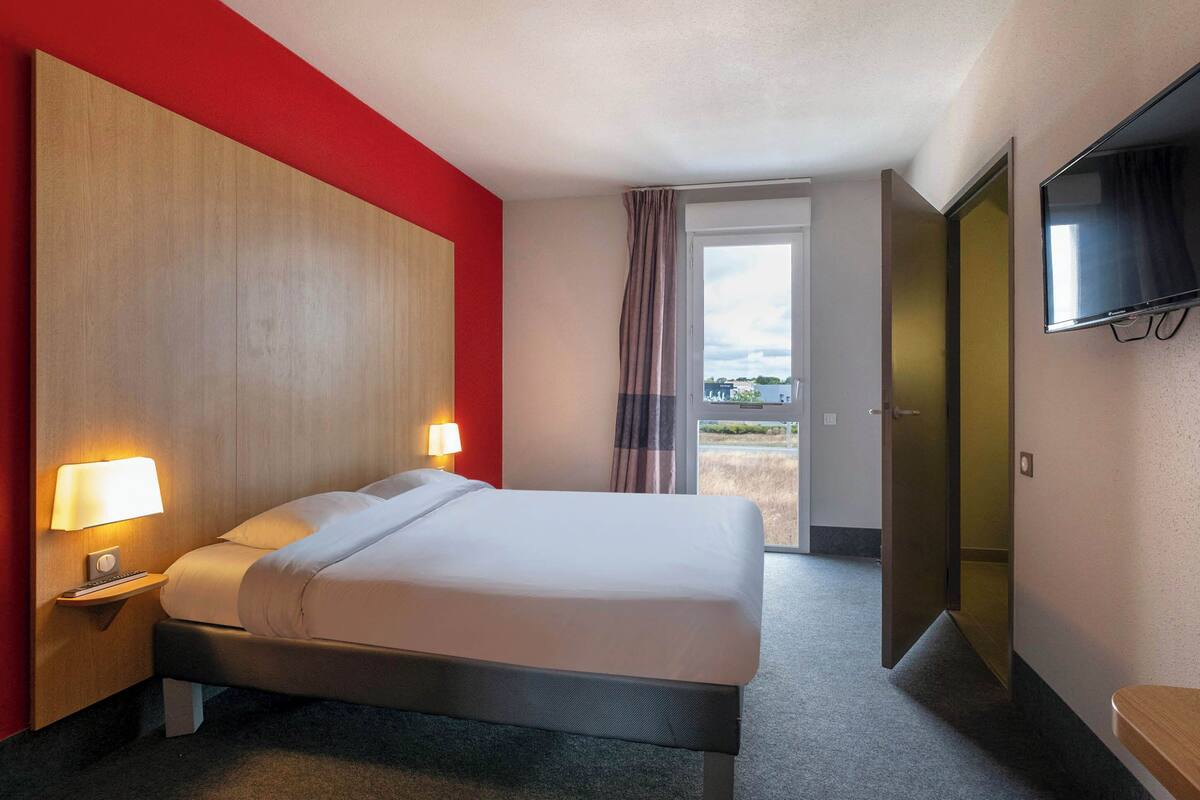 Ein Hotelzimmer mit einem Bett, Nachttischlampen, einem Fernseher und einer Tür, die auf einen Balkon führt.