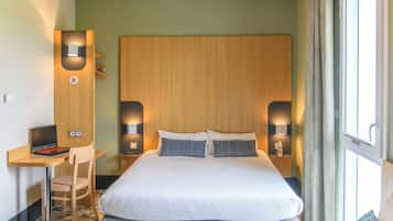 Habitación de hotel con una cama, un escritorio con una computadora portátil, dos lámparas de pared y un ventanal con cortinas.