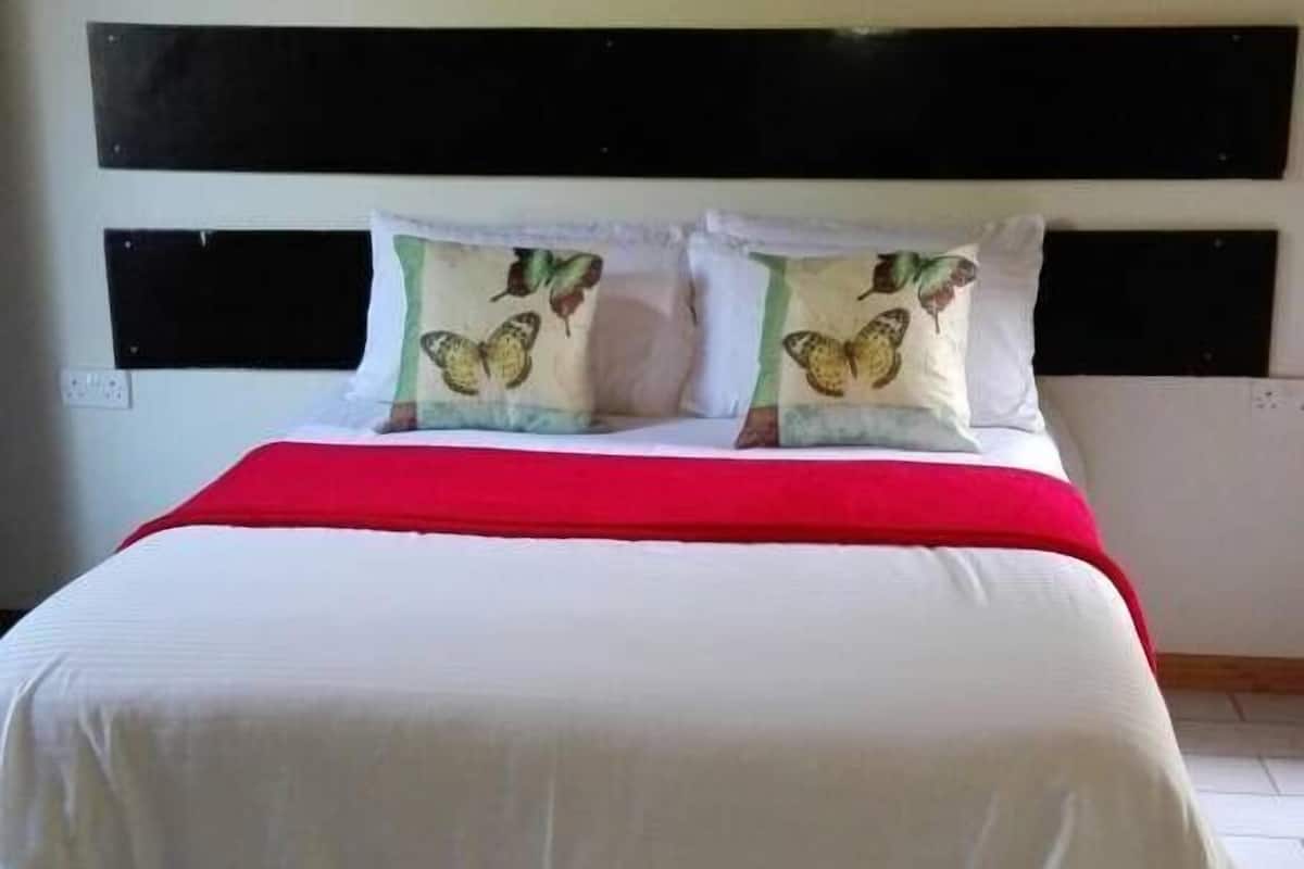 A bed with a red blanket, white bedding, and two pillows with butterfly designs.