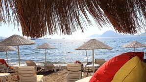 A beachside setting with lounge chairs, umbrellas, and a view of the sea. - Mer-Can Story Apart Hotel (Bodrum)