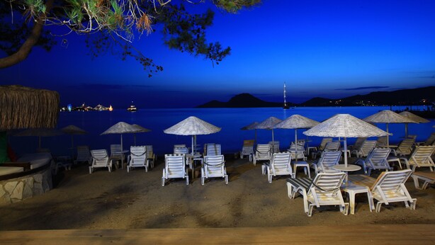 A beachside lounge area with lounge chairs and umbrellas, overlooking a body of water at night. - Mer-Can Story Apart Hotel (Bodrum)