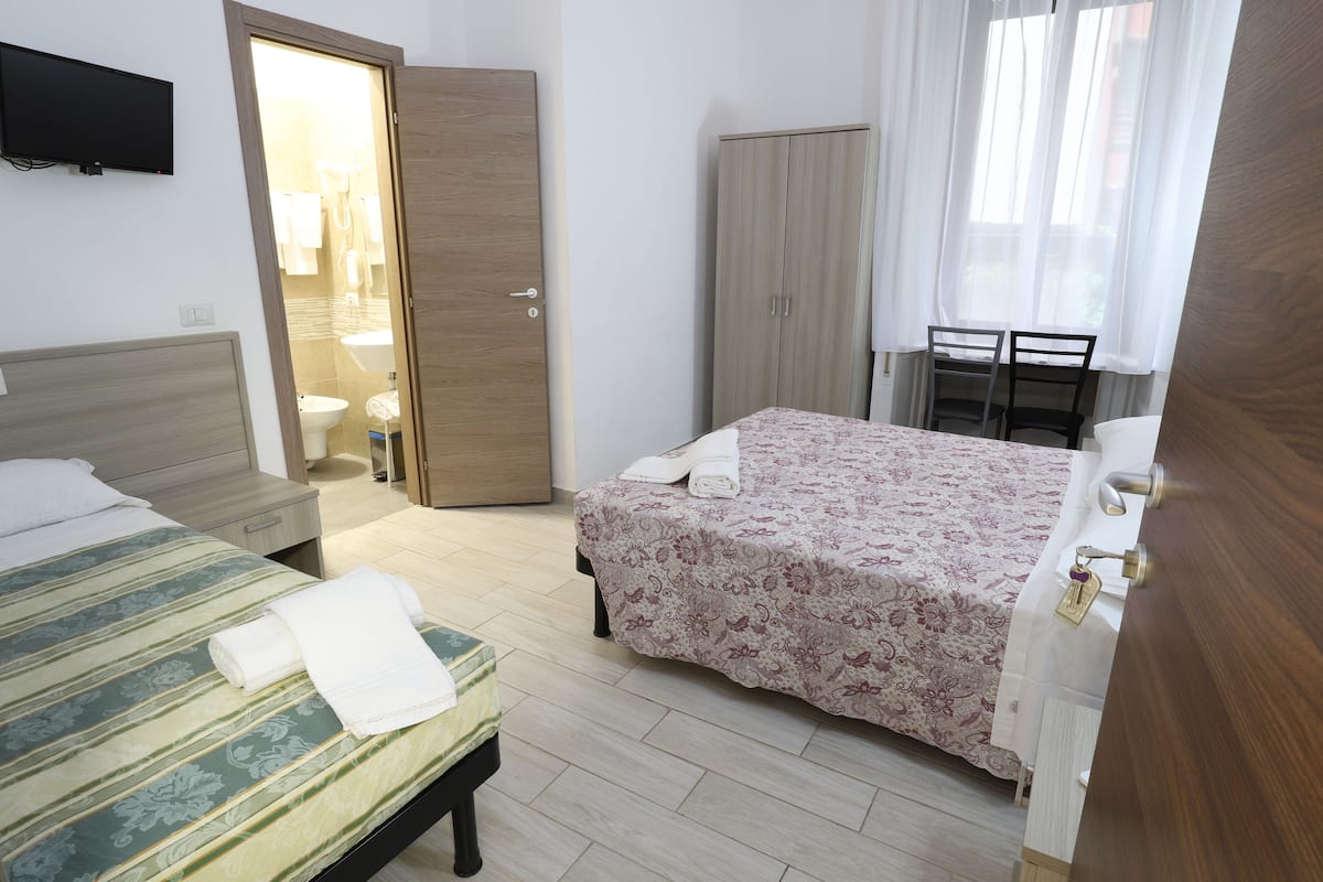 A bedroom with two beds, a wardrobe, a desk, and a bathroom visible through an open door.
