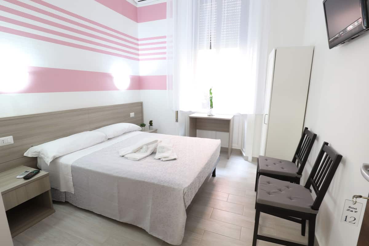 A hotel room with a bed, bedside table, nightstand, desk, chair, and a TV mounted on the wall.