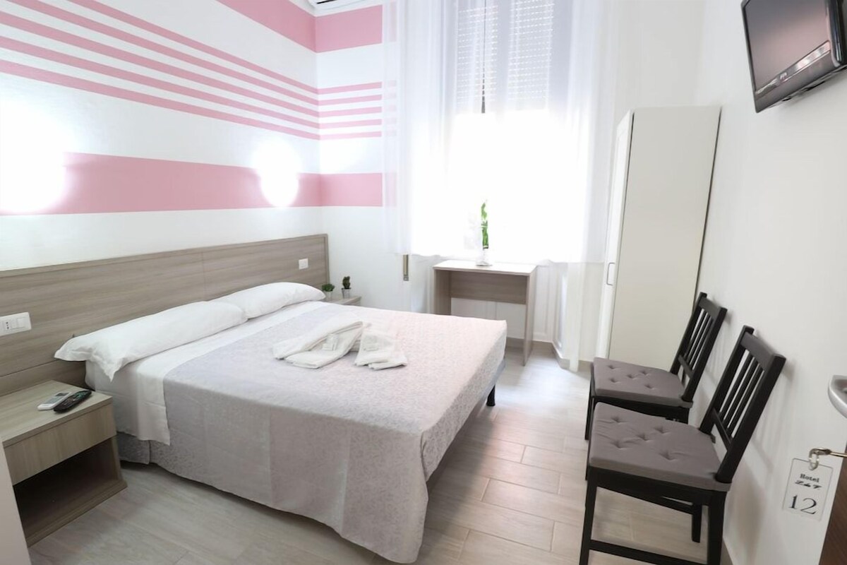 Una habitación de hotel con cama, mesita de noche, silla, escritorio y televisión.