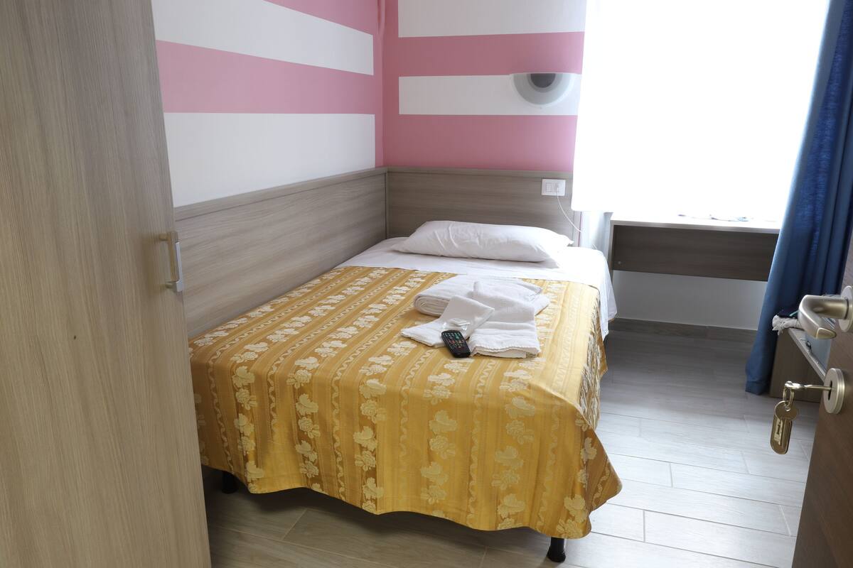 A single bed with a floral bedspread, a white pillow, and a remote control on the bed.