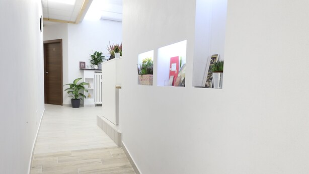A hallway with light wooden flooring, white walls, and a door marked with the number 14. There are potted plants and framed pictures on the walls. - Hotel Leonardo da Vinci (Milan)
