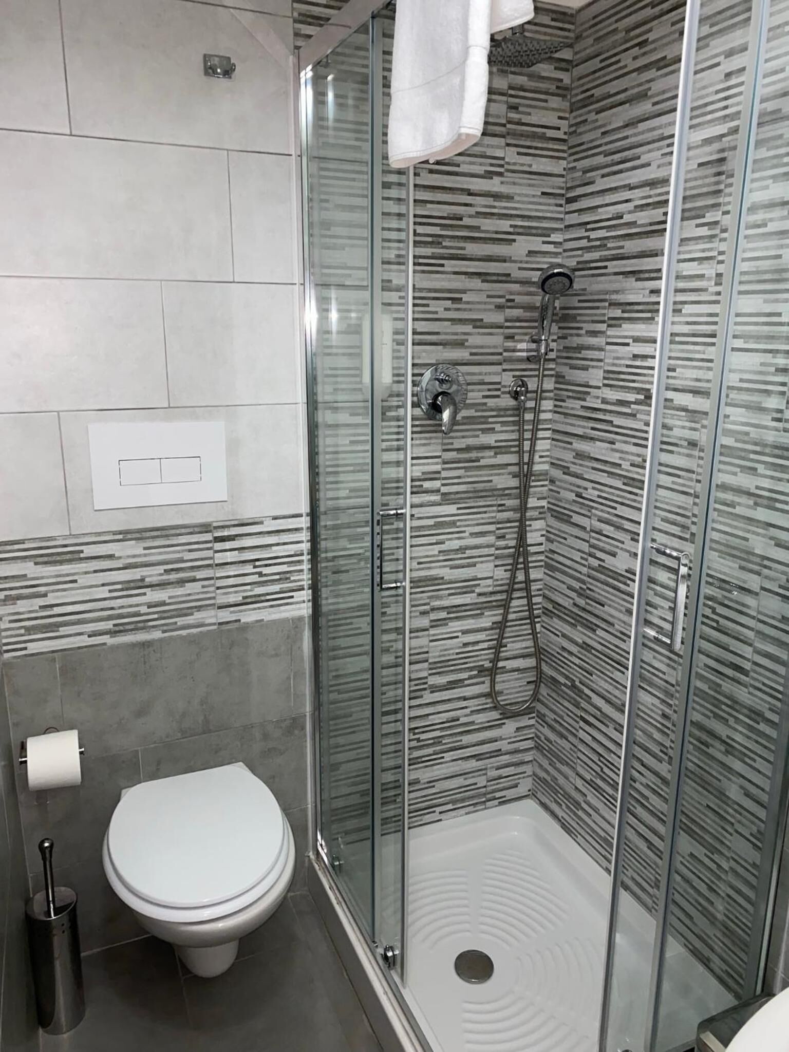Une salle de bain moderne avec une douche à parois de verre, des toilettes et une serviette accrochée au mur.