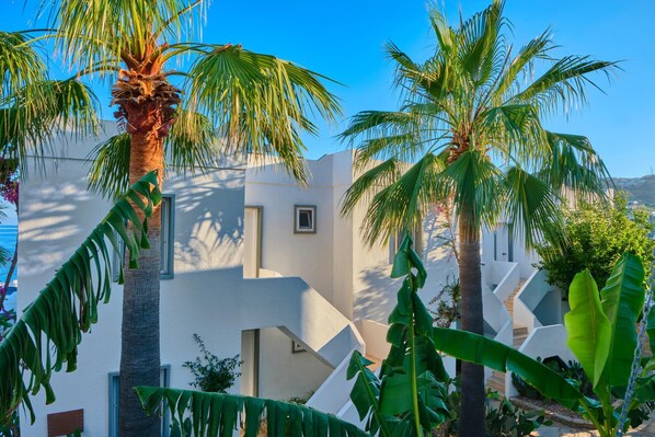 A modern building with white walls and a unique zigzag staircase design, surrounded by lush tropical plants. - YAZ Yalikavak (Bodrum)