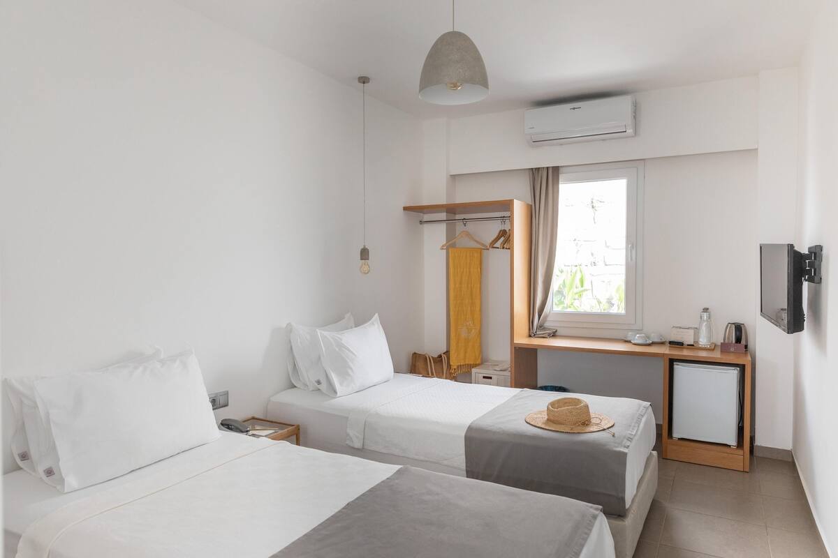 A hotel room with two beds, a desk with a mirror, a TV, and an air conditioning unit.