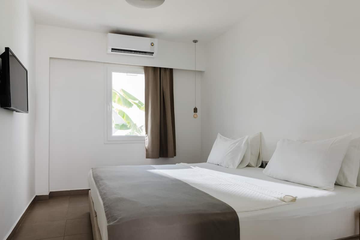 A hotel room with a bed, a TV, an air conditioning unit, and a window with curtains.