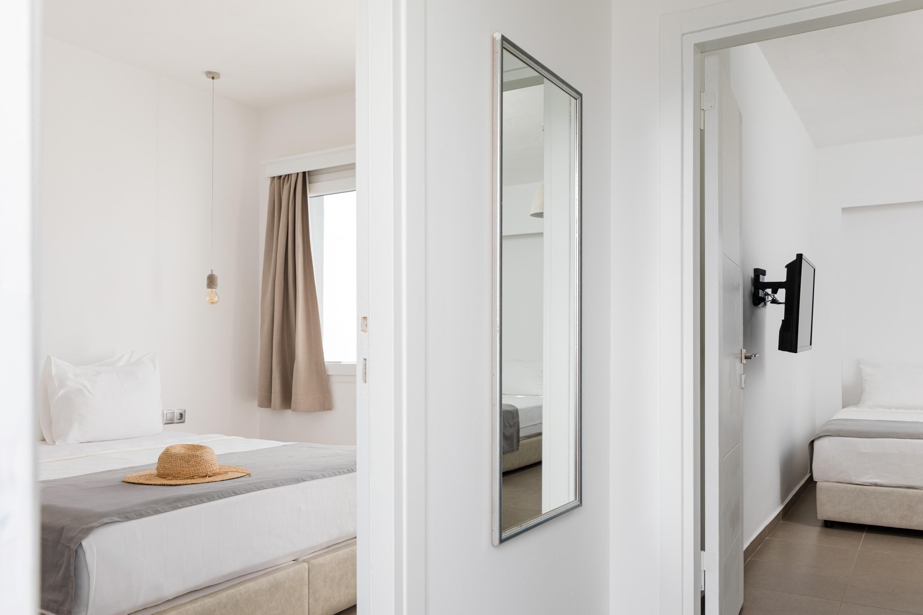 A hotel room with a bed, a mirror, a wall-mounted TV, and a window with curtains.